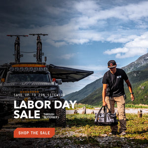 Man with a Rally Bag standing next to a truck with bicycles on top, in a mountainous landscape with Labor Day sale text overlay.